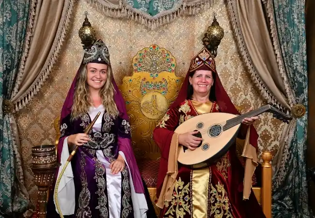 Two women wearing traditional Ottoman costumes, one holding an oud, in an ornate palace-style setting in Istanbul