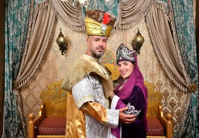 Couple wearing traditional Ottoman royal costumes posing in an ornate palace-style setting in Istanbul